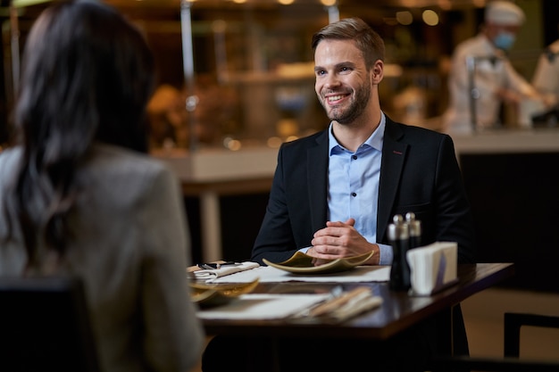 Male in business suit and shirt folding palms together on table and staring at his female companion