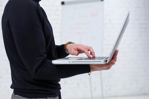 A male businessman manager smiles and stands with a laptop in his hands and looks at the screen. Stands on a white background.