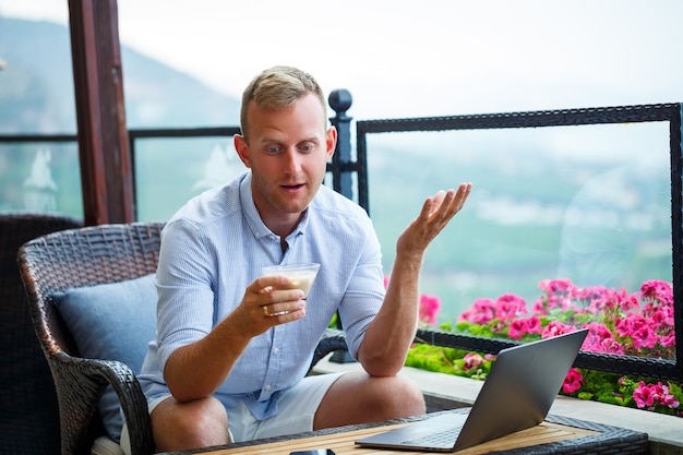 Male businessman working on laptop at rooftop cafe with beautiful panoramic view. Guy blogger drinks coffee and works on a computer while traveling