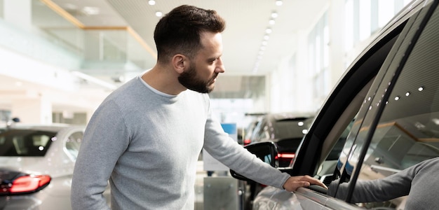 Male buyer chooses a new car in a car dealership inspects the car