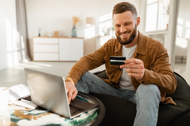 Male buyer using laptop and credit card shopping online indoors