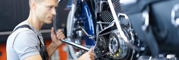 Male car mechanic holds wrench and looks at open motorcycle engine