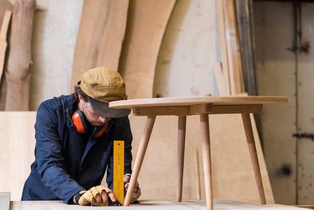 Male carpenter taking measurement of wooden table with ruler