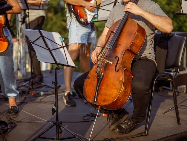 Male cellist playing violoncello in orchestra outdoors