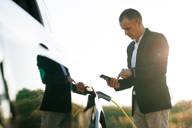 Male charging ev vehicle outdoors at sun light businessman unplugging zero emission electric car