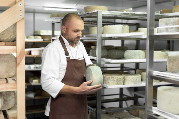 Male cheese maker checks the maturation of cheese on the shelves in the maturation and storage room