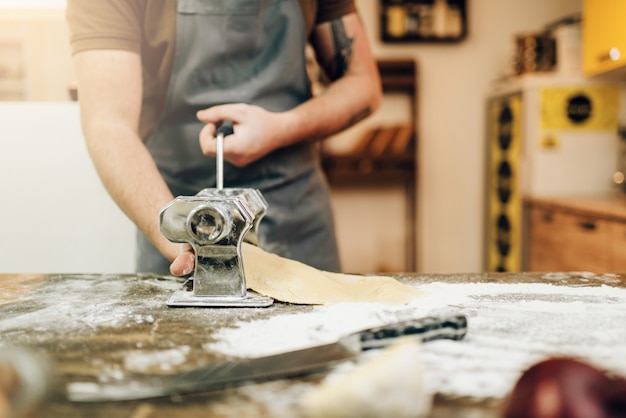 Male chef in apron works with pasta machine