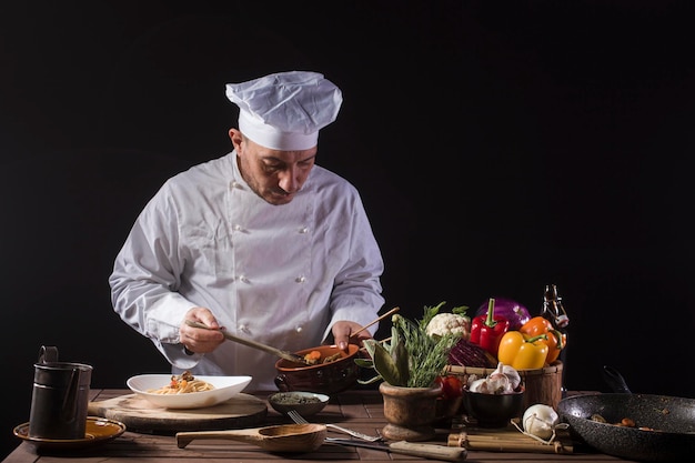 Male chef in white uniform prepares spaghetti with vegetables on the dish