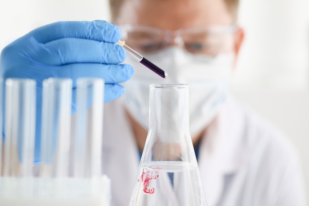 A male chemist holds test tube of glass in his hand overflows a liquid solution of potassium permanganate conducts an analysis of water samples versions of reagents using chemical manufacturing.