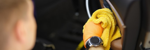 Male cleaner wiping dust in interior of car with microfiber cloth closeup