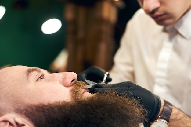 Male client with beard sitting in hairdresser chair Serious man with long brown beard Modern popular lumberjack style