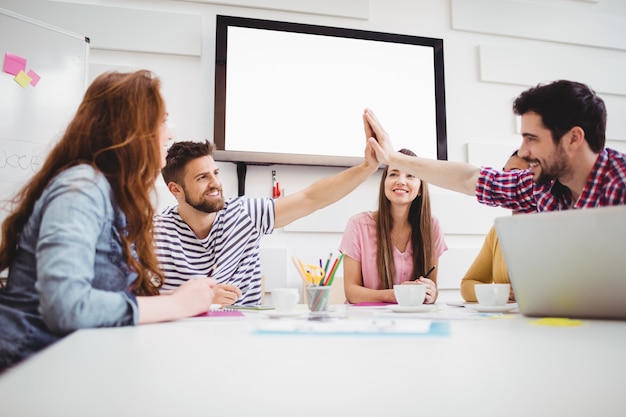 Male colleagues giving high-five in meeting at creative office