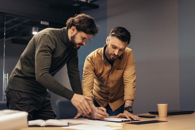 Male colleagues working on startup project taking notes during brainstorming discussion at modern office