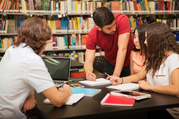 Male college student explaining some school work to his colleagues while studying in the library