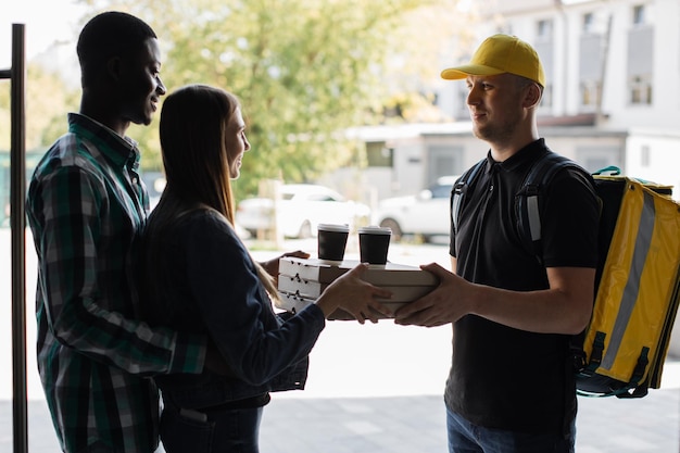 Male courier giving pizza boxes and takeaway coffee from restaurant to multinational family