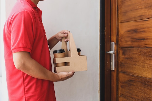 male courier in red uniform delivering coffee cups to customer in front of the house