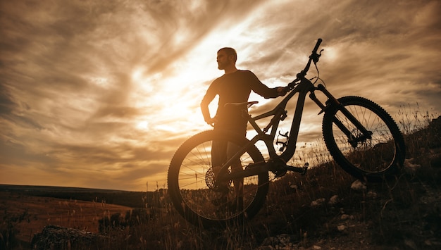 male cyclist standing with bike on slope of hill