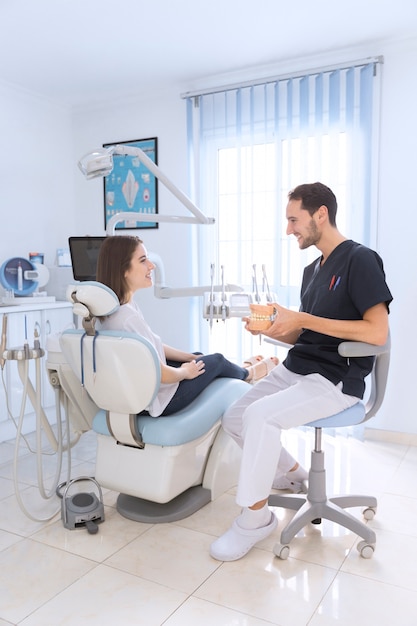 Photo male dentist showing teeth model to smiling patient in clinic