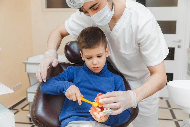 A male dentist shows a boy on a denture how to properly brush his teeth the concept of children's medical examination