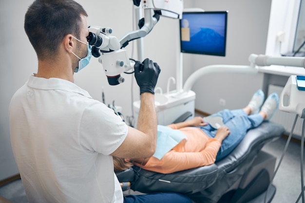 Male dentist using modern equipment during appointment with woman