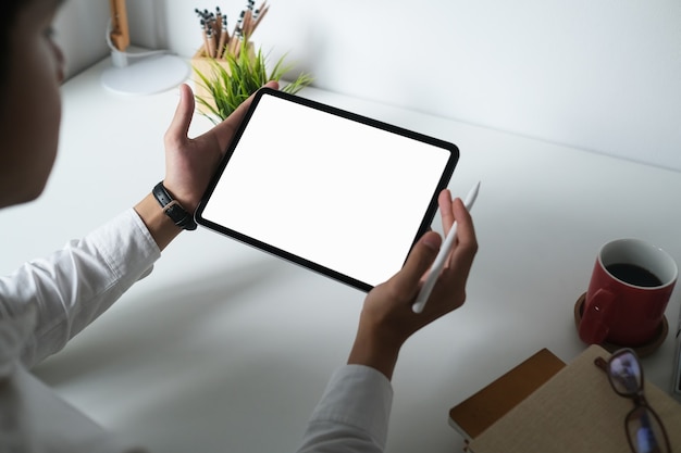 Male designer is using empty screen digital tablet with stylus pen on white desk