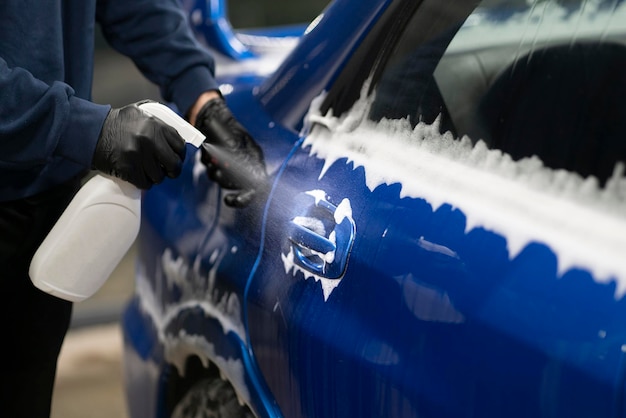 A male detailer doing work on the car cleaning machine and applying spray on the surface