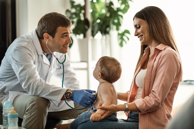 Male doctor examining baby boy with stethoscope and communicating with a mother