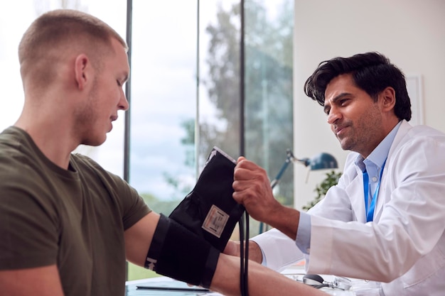 Male Doctor Or GP Examining Young Male Patient Taking Blood Pressure With Sphygmomanometer