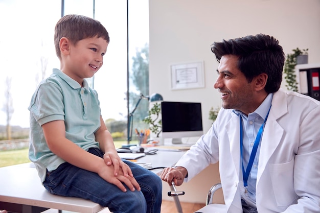 Male Doctor Or GP Wearing White Coat Examining Smiling Boy Testing Reflexes