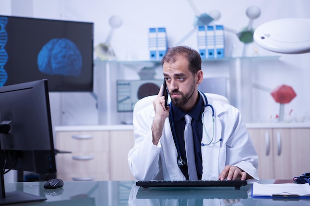 Male doctor having a video conference and talking on the phone with a patient. Focused doctor on his work.