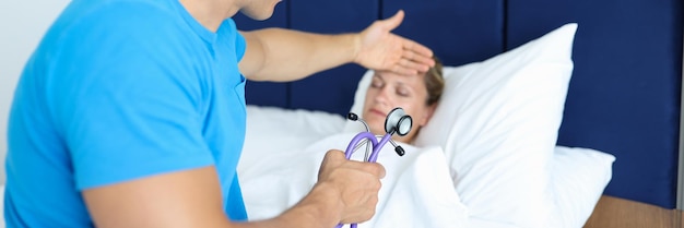 Male doctor holding stethoscope in his hands and touching forehead of sick patient hospital