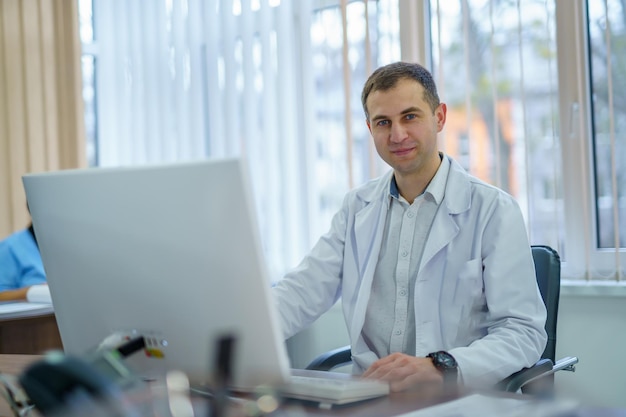 Male doctor is working in hospital office at computer. Medic in scrubs at clinic.