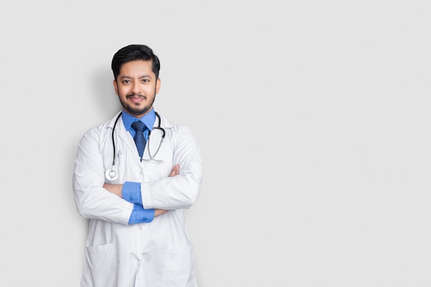 Male doctor portrait smiling with stethoscope and arm cross isolated on white wall. Health insurance concept.