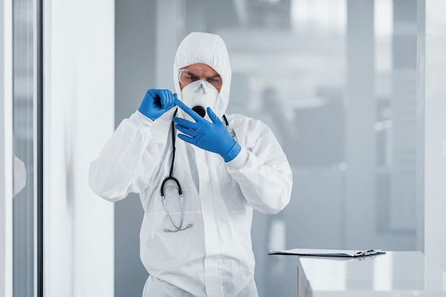 Male doctor scientist in lab coat, defensive eyewear and mask taking off blue gloves