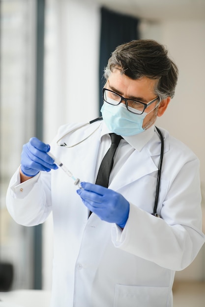 Male doctor wearing uniform mask medical gloves holding syringe taking covid 19 corona virus vaccine from vial bottle preparing for injection Coronavirus immunization flu treatment vaccination