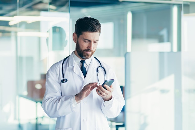 Male doctor in a white coat in a modern clinic reads information from a mobile phone corresponds with colleagues happy and smiles