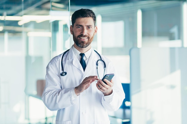 Male doctor in a white coat in a modern clinic reads information from a mobile phone corresponds with colleagues happy and smiles