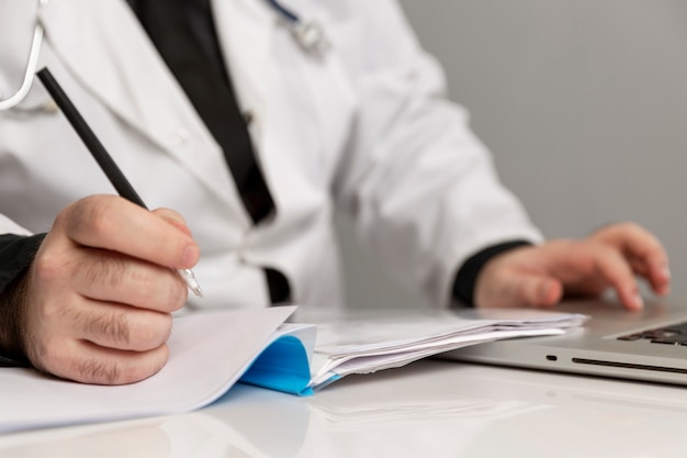 male doctor in a white coat works in a computer and takes notes. Close-up.