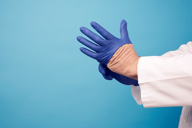 Photo male doctor in white uniform puts on his hands blue sterile latex gloves