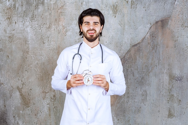 Male doctor with a stethoscope holding an alarm clock. 