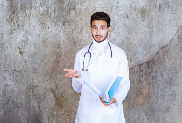 Male doctor with stethoscope holding a blue folder and interacting with the person around.