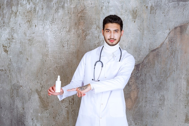 Male doctor with stethoscope holding a white hand sanitizer bottle.