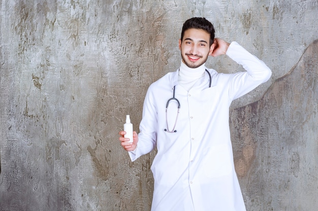 Male doctor with stethoscope holding a white hand sanitizer bottle