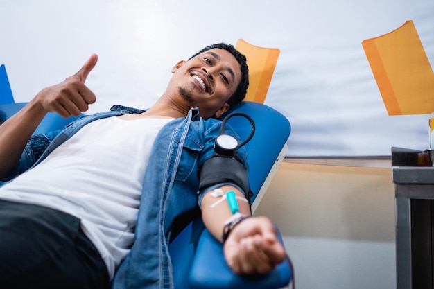 Male donor lying smiling to camera with thumbs up during blood transfusion in hospital room