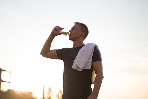 The male drinks water after a workout at sunset or sunrise lower angle