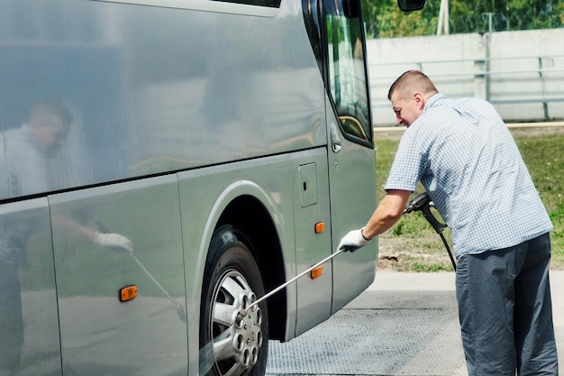 Male driver washes large bus on summer day at open car wash Service or service for washing large vehicles