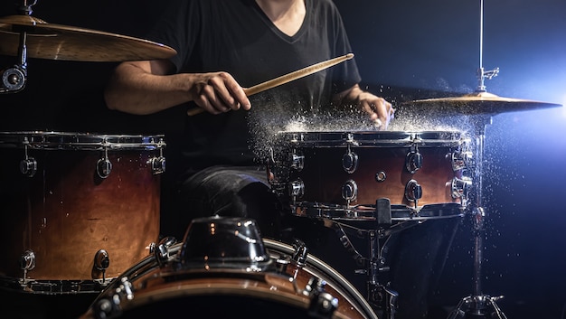 A male drummer plays drum sticks on a snare drum with splashing water in a dark room.