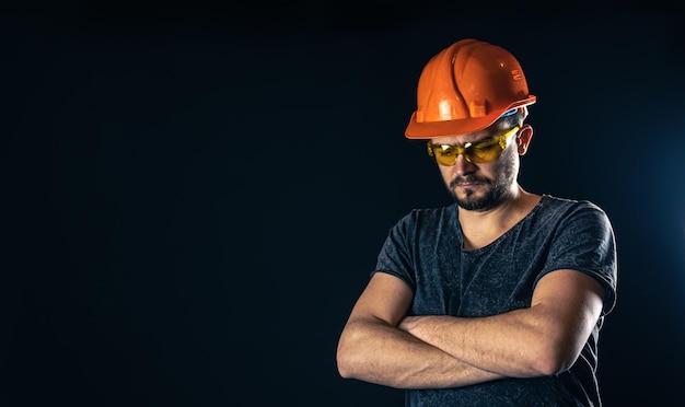 Male electrician in a protective helmet with glasses on a black background