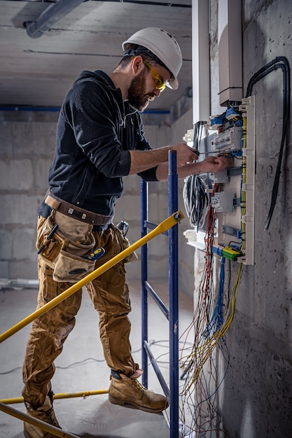 A male electrician works in a switchboard with an electrical connecting cable.