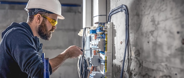 A male electrician works in a switchboard with an electrical connecting cable